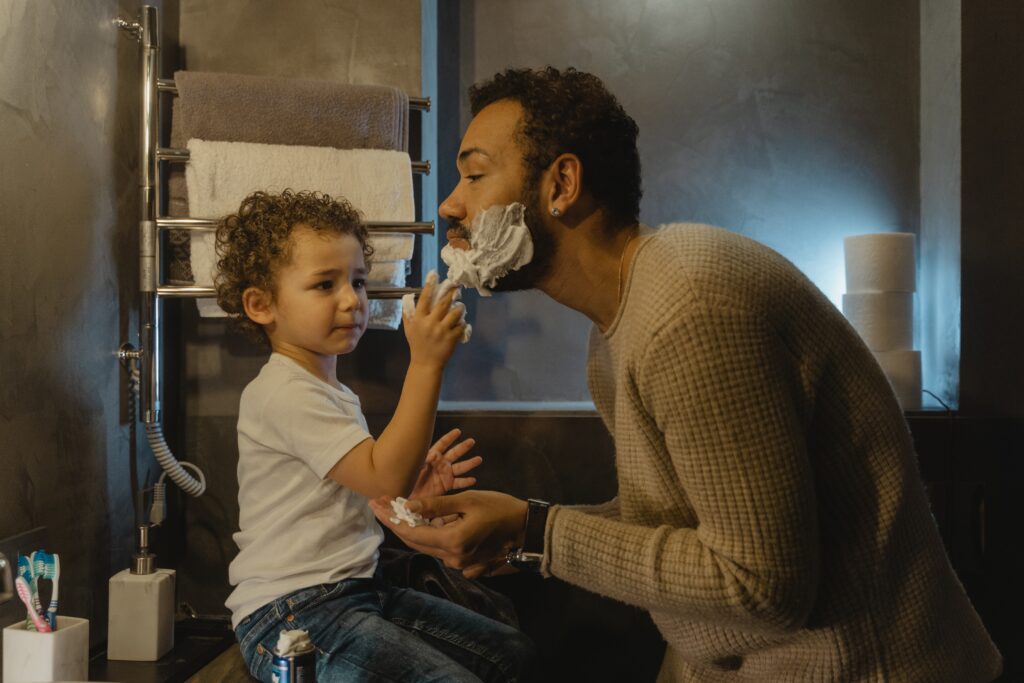 Ein Mann rasiert sich den Bart neben seinem kleinen Sohn