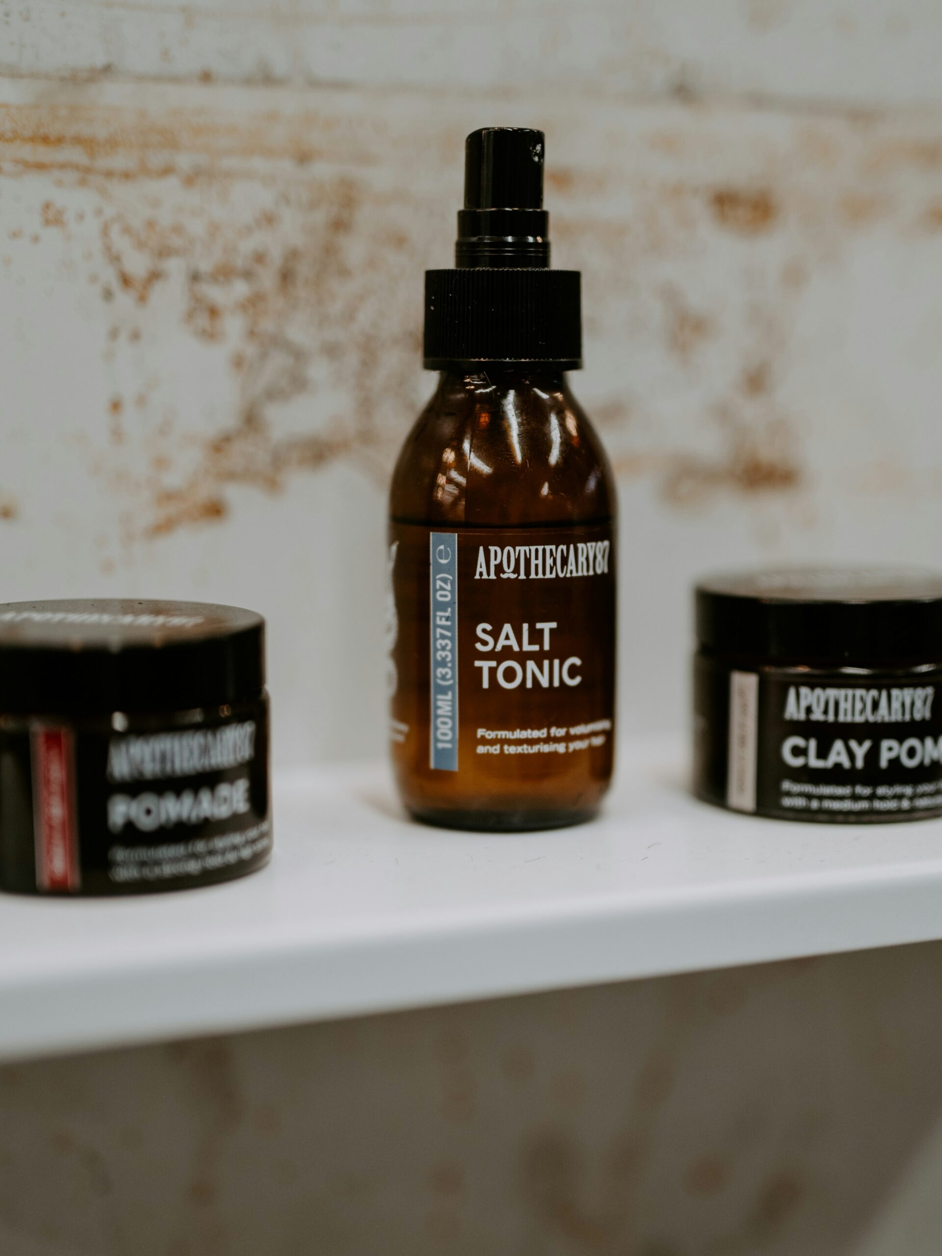 Verschiedene Haarstylingprodukte für Vokuhila-Frisuren in braunen Behältern auf einem weißen Regal.