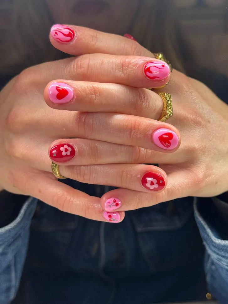 Zusammengelegte Hände einer Frau mit leuchtend pinker und roter BIAB-Maniküre mit Nail Art