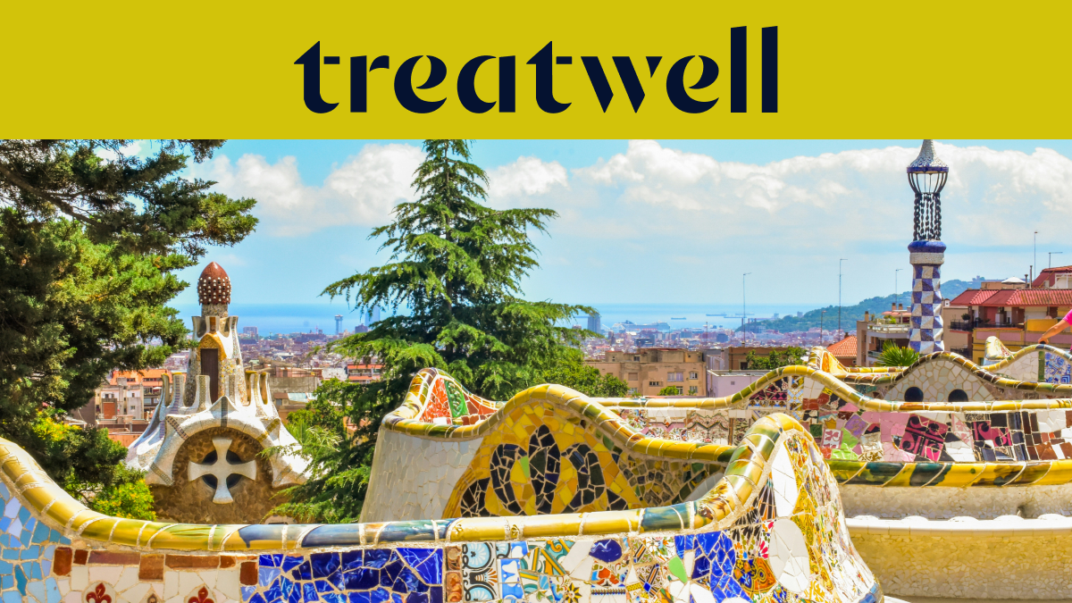 Ein malerischer Blick auf Barcelona vom Park Güell aus, mit Antoni Gaudís berühmten bunten Mosaikbänken und märchenhaften Türmen im Vordergrund, dahinter die Stadt und das Meer. Ein gelbes Banner am oberen Rand zeigt das „treatwell“-Logo.