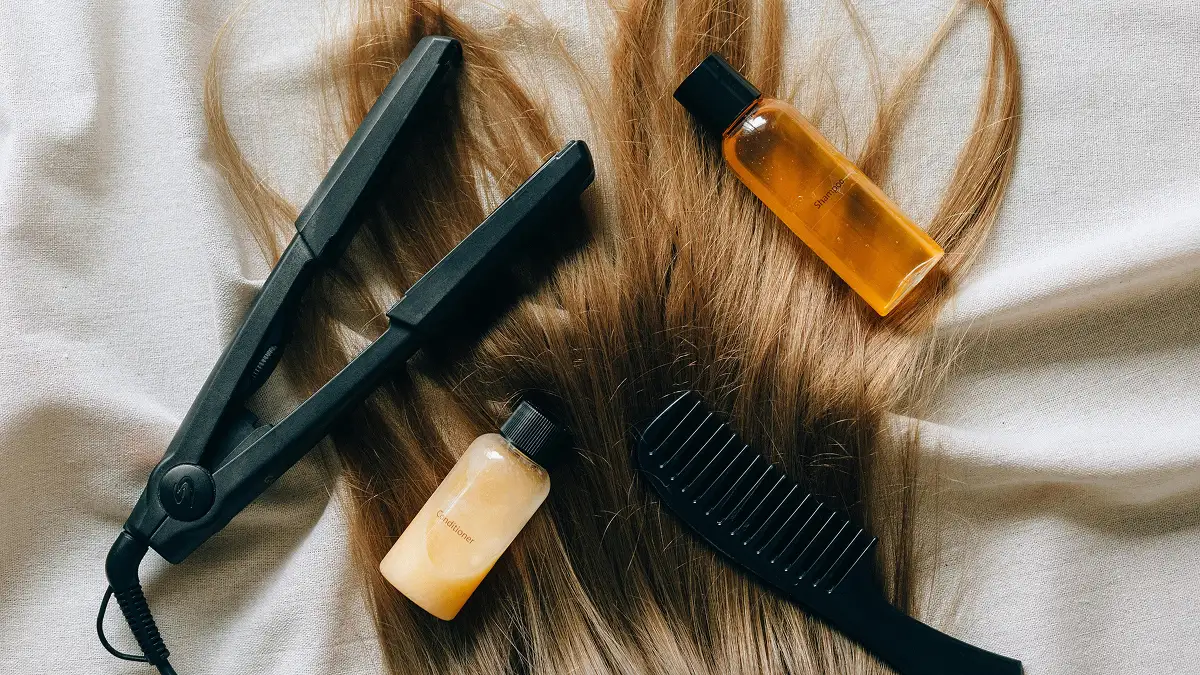 Flatlay von Haarpflegeprodukten auf langem, glattem Haar, darunter Shampoo, Spülung, Glätteisen und ein grobzinkiger Kamm