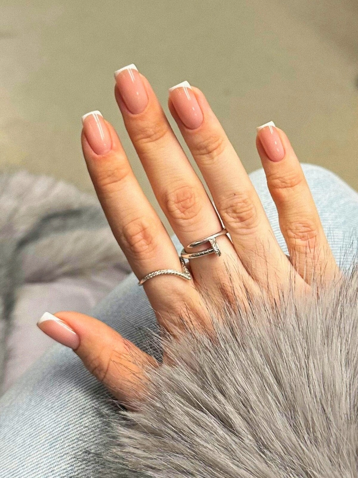 Die Hand einer Frau mit einer French-Tips-Maniküre mit Mikro-Linien auf eckigen Nägeln