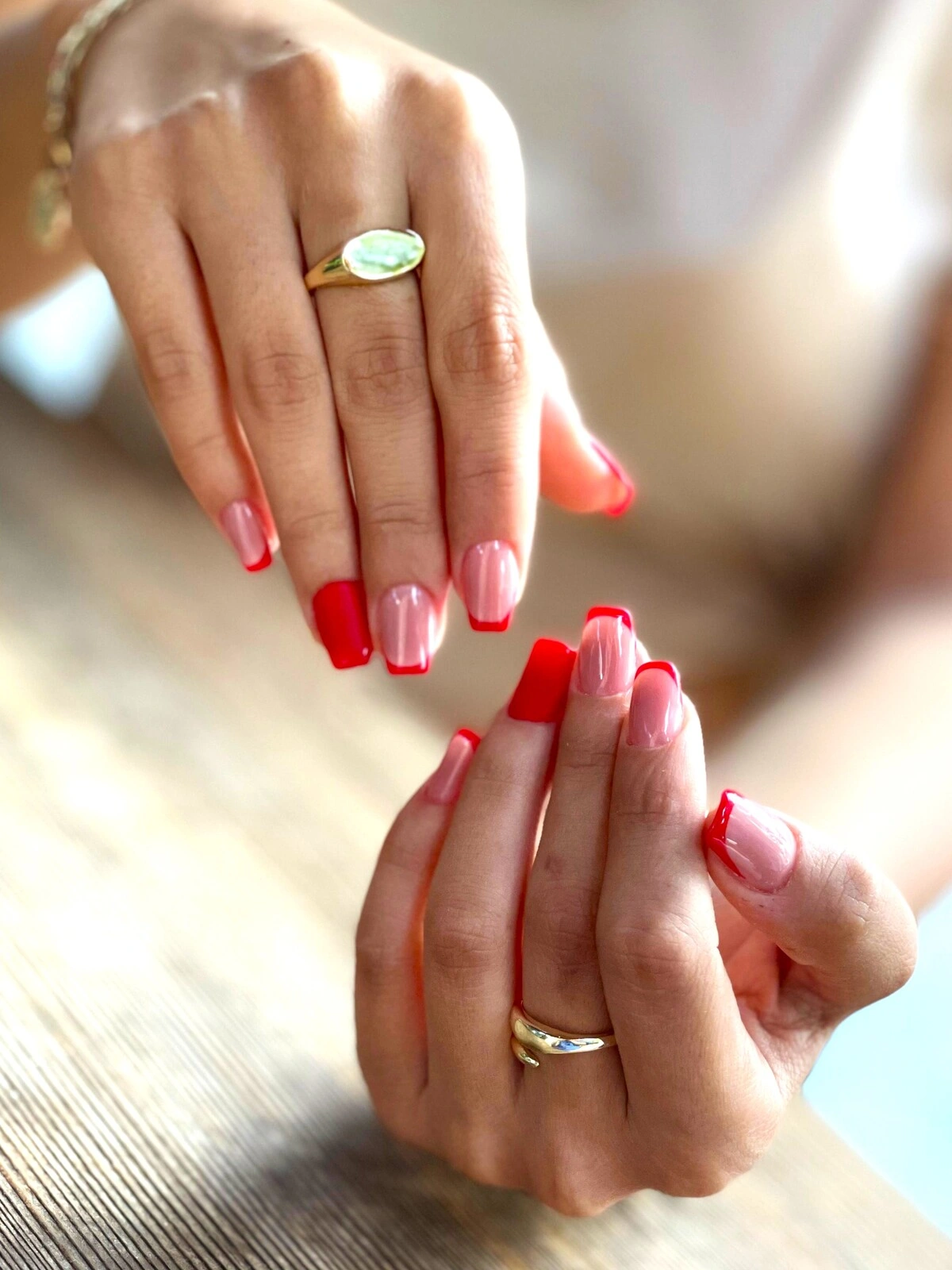 Eine French-Tips-Maniküre auf eckig-ovalen Nägeln mit zartrosa Basis und roten Spitzen sowie komplett roten Ringfingernägeln