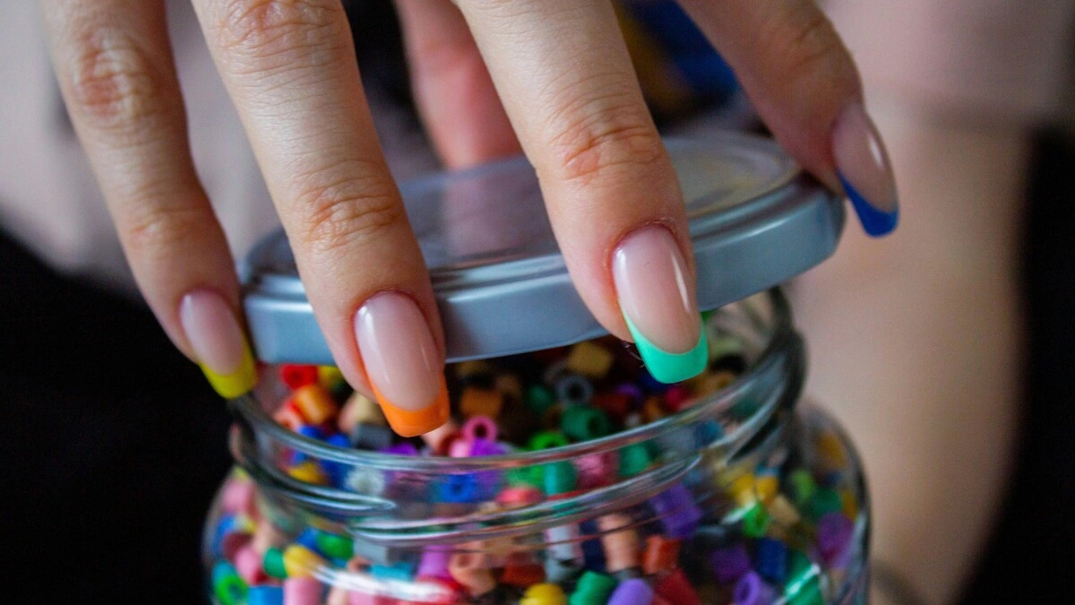 Die Hand einer Frau mit einer French-Tips-Maniküre mit transparenter Nude-Basis und bunten Spitzen