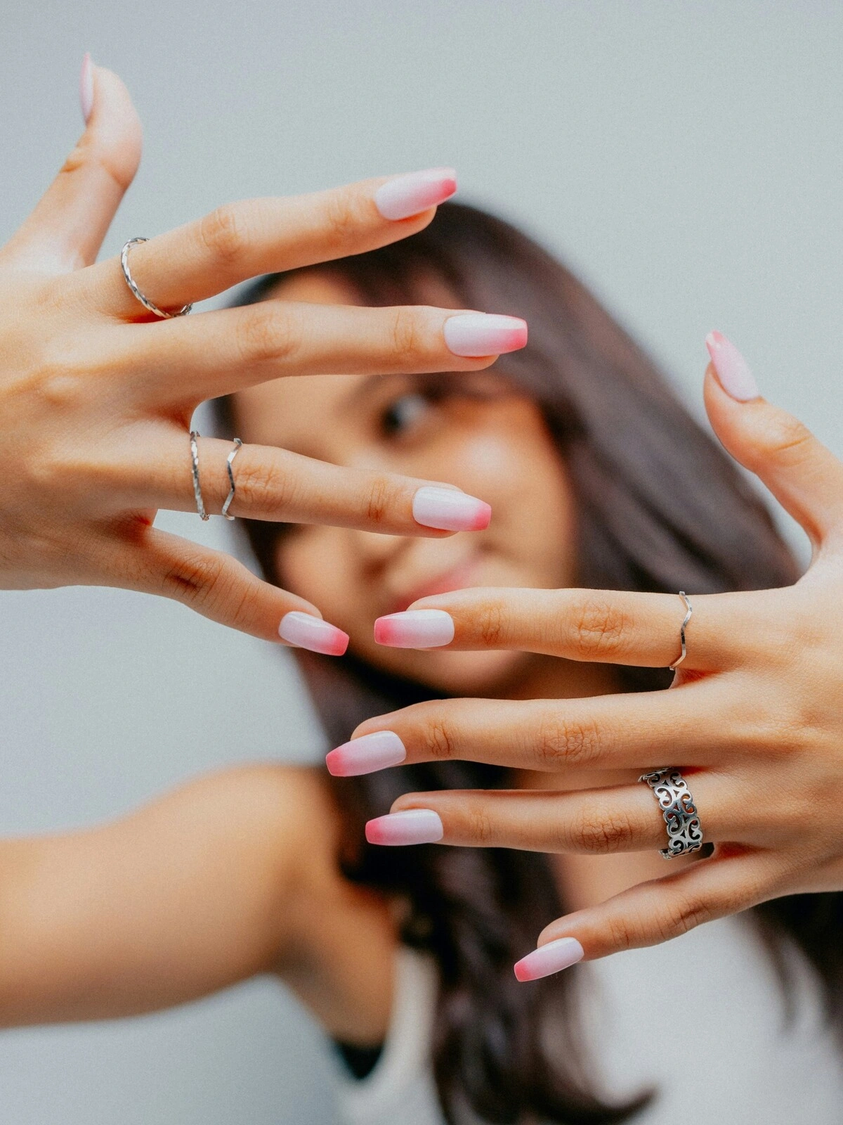 Eine Frau hält ihre Hände in die Kamera und zeigt eine French-Tips-Maniküre im Ombré-Look mit zartrosa Basis und knallpinken Spitzen auf Coffin-Nägeln