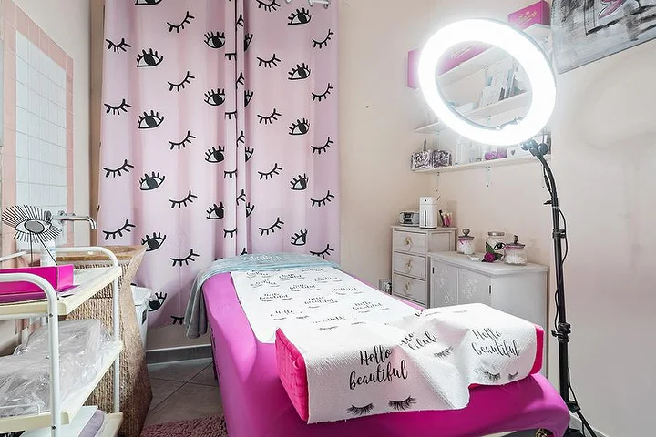 Rosa Behandlungsraum bei Centro Estetico Karma in Olbia mit Wimpern-Print-Vorhängen, Beauty-Liege und Ringlicht.