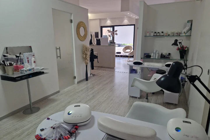 Empfang und Nagelbereich bei Estetica Francesca in Olbia mit rundem Wandspiegel und Glasregalen voller Beauty-Produkte.