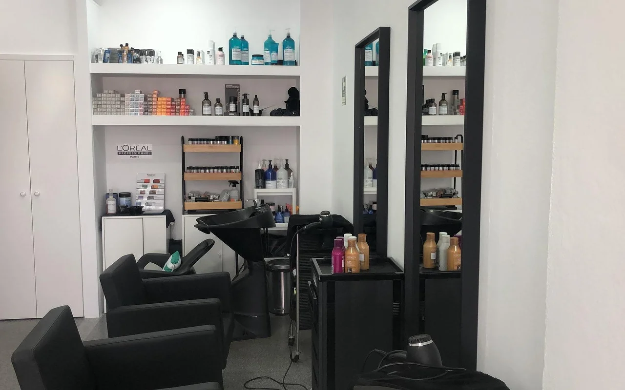 Ein Friseursalon mit schwarzen Waschstühlen und -becken, zwei hohen, schmalen Wandspiegeln und Regalen voller professioneller Farb- und Haarpflegeprodukte.