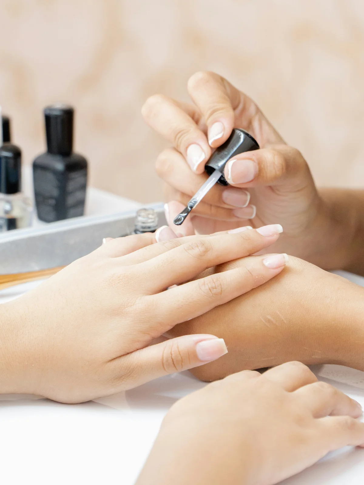 Nahaufnahme einer Nagelstylistin, die eine transparente kräftigende Behandlung auf die Nägel einer Kundin im Salon aufträgt