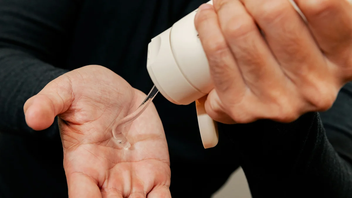 Nahaufnahme der Hände eines Mannes, der mit einer Hand eine weiße Tube Feuchtigkeitsgel in die andere Hand drückt