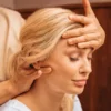 Nahaufnahme einer Frau mit geschlossenen Augen, während eine Fachkraft bei einer indischen Kopfmassage eine Hand auf ihre Stirn legt und mit der anderen ihren Nacken massiert