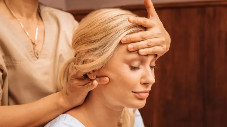 Nahaufnahme einer Frau mit geschlossenen Augen, während eine Fachkraft bei einer indischen Kopfmassage eine Hand auf ihre Stirn legt und mit der anderen ihren Nacken massiert