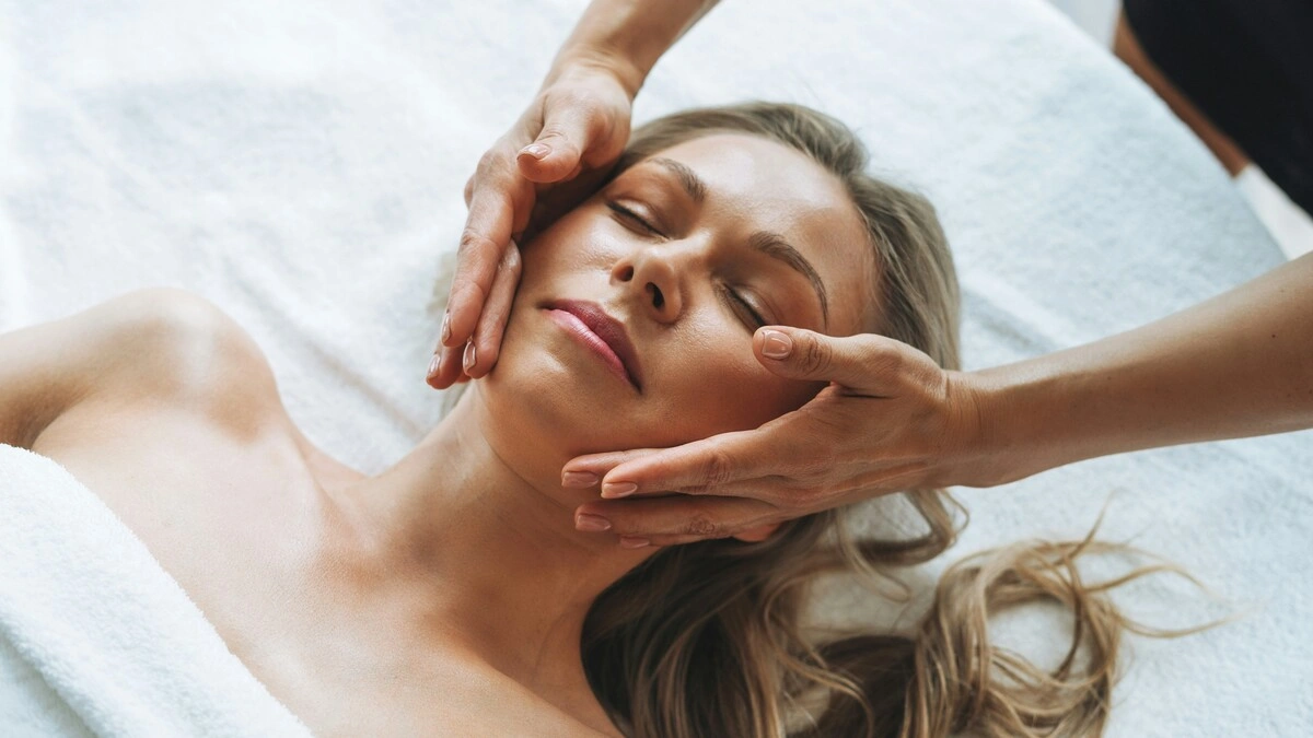Frau entspannt während einer sanften Lymphdrainage im Gesicht, während die Hände der Fachkraft leicht über ihre Wangen gleiten